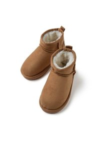 Botas de tobillo de ante marrón con forro blanco esponjoso, punta redondeada y detalle decorativo de correa. Textura suave y suela flexible.