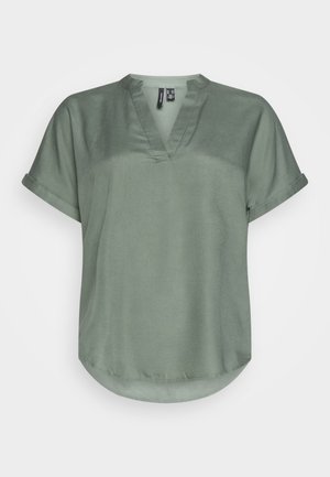 Blouse vert clair à manches courtes avec des poignets roulés et un col en V sur fond blanc uni.