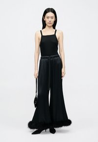 Crni top s tankim naramenicama u kombinaciji sa širokim crnim hlačama koje imaju lažni krzneni rub na rubu. Model drži malu crnu torbicu.