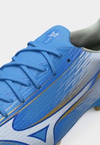 Μπλε και λευκό παπούτσι ποδοσφαίρου με χρυσές λεπτομέρειες και μπλε κορδόνια, με το λογότυπο "Elite" στη γλώσσα.