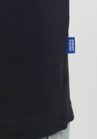 Marinblå bomullströja med rak passform; har en blå varumärkesetikett sydd på sidan. Slät textur och enkel design.