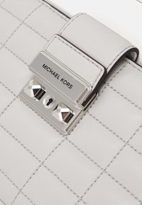 Borsa a tracolla in pelle grigia chiara con un design trapuntato, una chiusura in tono argento con dettagli a rivetto e una targa logo vicino alla chiusura.