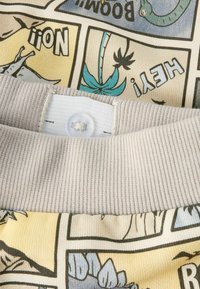 Bluza bawełniana z wzorami przypominającymi komiks w pastelowych kolorach, z beżowym żebrowanym kołnierzem i zapięciem na guziki z tyłu.