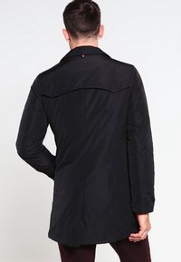 Černý lehký kabát s límcem, detailem zadního sedla a dlouhými rukávy; má rovný střih a jemnou texturu.