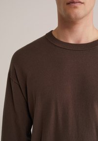 Pull marron à manches longues avec col rond, texture douce, col côtelé et design minimaliste, adapté pour un port décontracté.