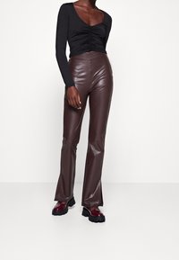 Svart långärmad topp med samlad detalj framtill, tillsammans med bruna faux läder byxor med utsvängd design och sidofickor, samt kraftiga svarta stövlar.