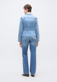 Τζιν μπουφάν με εφαρμοστή μέση, μακριά μανίκια και γιακά. Η πλάτη έχει εφαρμοστή σχεδίαση και ελαφρώς φαρδύ τελείωμα. Φωτεινό μπλε χρώμα.