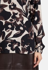 Long-sleeve blouse featuring a floral print in shades of brown and cream. Soft fabric with a gathered cuff and a relaxed fit.