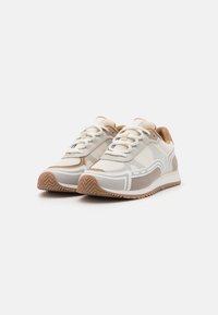 Sneakers in rete beige con accenti bianchi, superficie testurizzata, colletto color cammello imbottito e suola in gomma con motivo a zigzag.