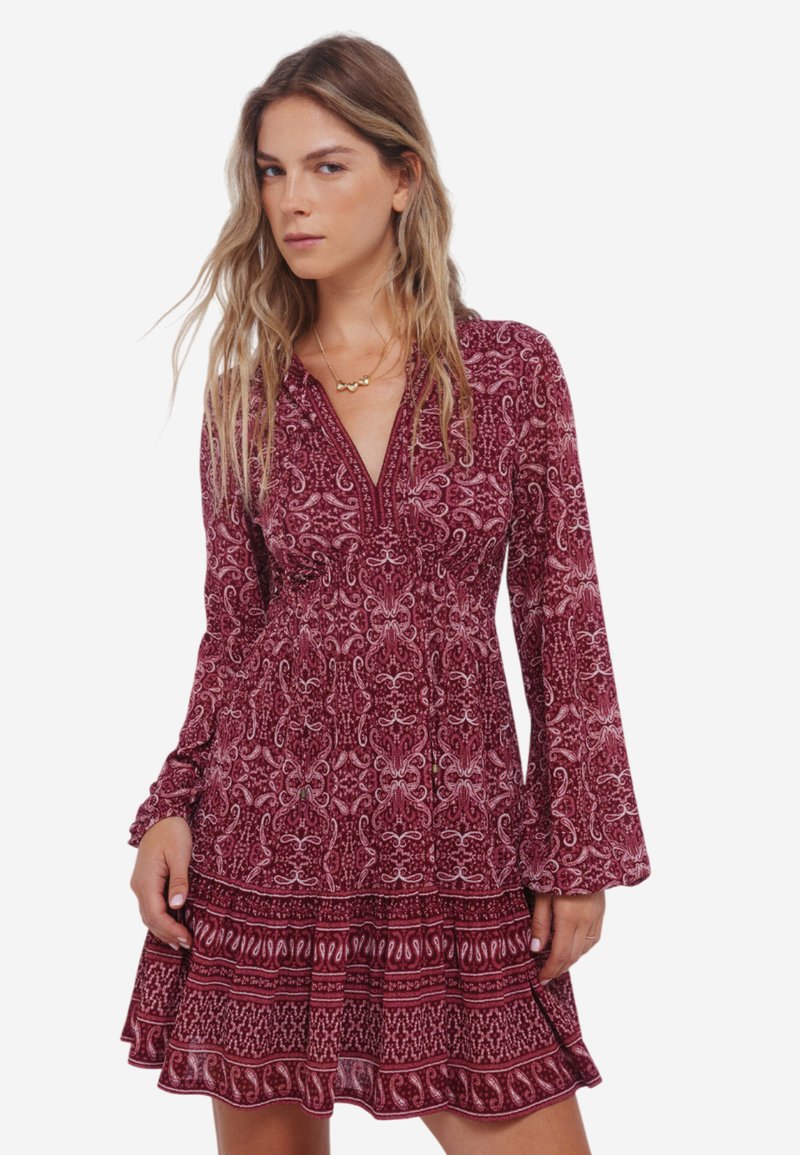 Langermige jurk in bordeauxrood met een witte paisleyprint, voorzien van een V-halslijn en uitlopende mouwen, textuurrijk rokje met ruches aan de onderrand.