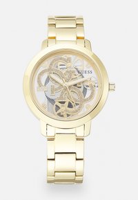 Gold-tone watch with a transparent skeleton dial displaying intricate gears and a branded design. Metallic band features polished, linked segments.
