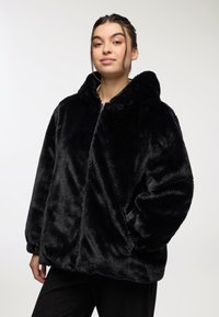 Giacca nera in pelliccia sintetica con cappuccio, chiusura frontale con zip, vestibilità ampia e texture morbida, dotata di maniche ampie e tasche laterali.