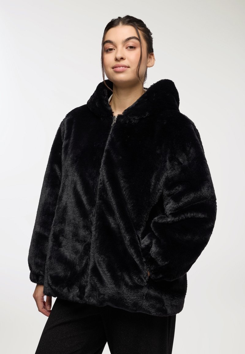 Giacca nera in pelliccia sintetica con cappuccio, chiusura frontale con zip, vestibilità ampia e texture morbida, dotata di maniche ampie e tasche laterali.