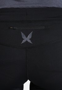 Černé legíny s hladkou a pružnou texturou; mají kapsu na zip a nenápadný design loga ve tmavším odstínu.