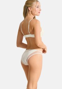 Crèmekleurige bralette en bijpassende slipjes met kantdetails. De bralette heeft verstelbare bandjes en een gestructureerd bloemenpatroon.