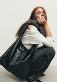 Borsa tote in pelle nera con una texture liscia e apertura ampia. Presenta cuciture sottili e nessuna ferramenta visibile. Dimensioni medie, design non strutturato.