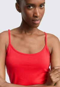 Rode mouwloze tanktop van gladde, rekbare stof met dunne bandjes en een ronde halslijn, die de hals en schouders accentueert.