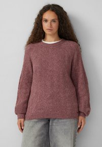 Strickpullover in bordeauxrot mit strukturiertem Muster, rundem Ausschnitt und überschnittenen Schultern. Kombiniert mit hellgrauen, baggy Hosen.
