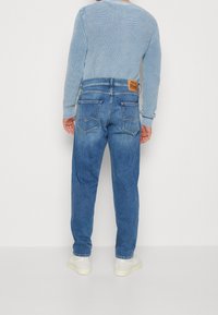 Niebieskie jeansy z denimu o luźnym kroju i delikatnym blaknięciu. Posiadają dwie tylne kieszenie oraz brązową skórzaną naszywkę na pasku w talii.