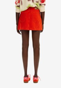 Mini-jupe en denim rouge à la coupe ajustée avec deux poches arrière, associée à des chaussures roses avec des lacets contrastants et une semelle texturée.