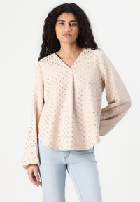 Blusa a maniche lunghe rosa chiaro con scollatura a V, caratterizzata da motivi metallici dorati e una vestibilità rilassata che si allarga alle maniche.
