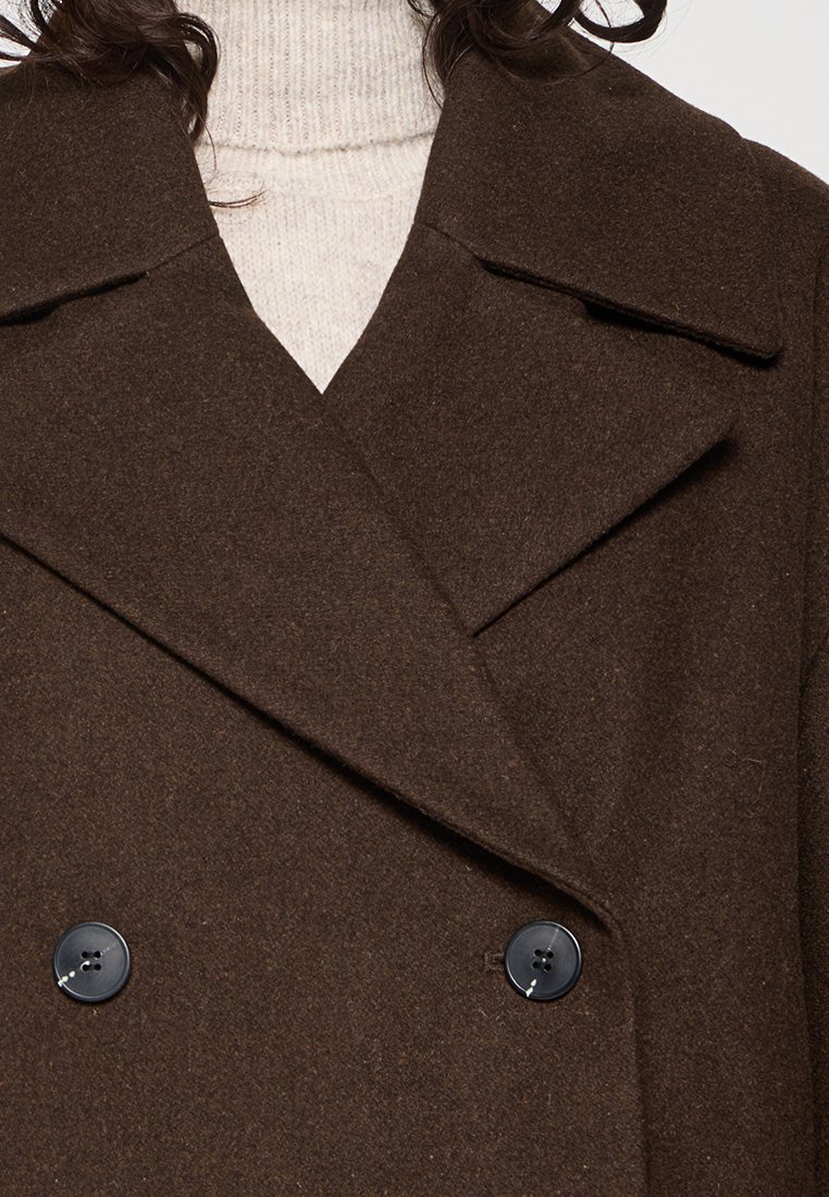 Cappotto peacoat in misto lana marrone scuro, con ampi revers, design doppiopetto e bottoni in plastica nera. Tessuto testurizzato con una finitura liscia.