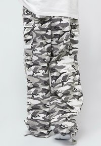 Maskáčové cargo kalhoty v odstínech šedé a bílé, s velkými bočními kapsami, šňůrkou na lemu a volným střihem.