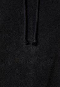 Close-up van zwarte stof met twee zwarte trekkoorden die naar beneden hangen, met een zachte, gestructureerde materiaal.