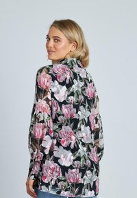 Blusa floreale realizzata in un tessuto nero trasparente, con motivi di peonie rosa e bianche. Maniche lunghe e colletto alto.