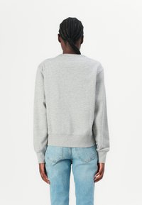 Grijze sweatshirt met een ronde halslijn, ribbelboorden en een ribbelrand. Het materiaal lijkt zacht. Draagt met lichtblauwe spijkerbroek.