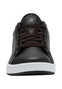 Musta nahkakengät ruskeilla nauhoilla, rei'itetyt sivupaneelit, valkoinen kumipohja ja pyöreä logo kielen päällä.