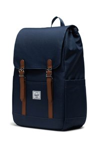 Mochila azul marino con cierre de solapa, tiras y detalles de cuero marrón, y un bolsillo frontal. Hecha de una tela duradera, cuenta con una etiqueta de logotipo.