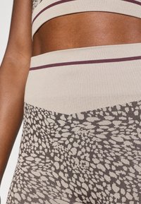 Μπέζ αθλητικό crop top και κολάν ψηλής μέσης με υφή λεοπαρντί και σκούρες καφέ λεπτομέρειες και ραμμένα σχέδια.