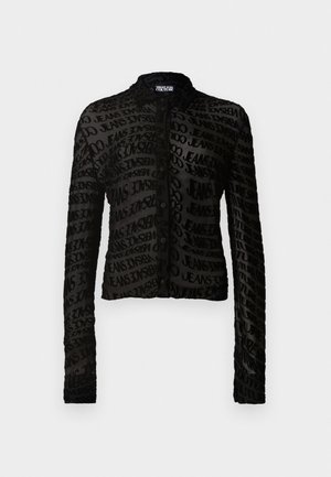 Veste noire courte en tissu transparent, arborant un motif de texte répété. Elle dispose de manches longues et d'une simple fermeture à bouton à l'avant.