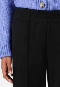 Svarte bukser med elastisk midje, sammen med en lavendelstrikket genser med en rund knapp. Stoffet ser glatt og mykt ut.