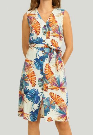 Robe sans manches longueur genou avec imprimé multicolore de feuilles tropicales, boutonnière sur le devant et ceinture en tissu portée par une femme les mains dans le dos.