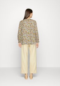 Blusa com padrão floral, mangas longas, punhos franzidos e um corte solto. Combinada com calças de perna larga na cor creme e sapatos claros.