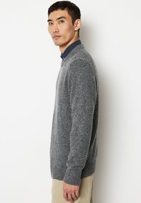 Grauer Strickpullover mit strukturierten Oberflächen, Rundhalsausschnitt und gerippten Bündchen, über einem dunklen Hemd mit Kragen getragen, seitlich gezeigt.