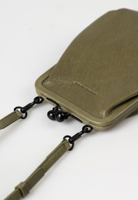 Pochette in pelle verde oliva con una finitura testurizzata, dotata di accessori neri e tracolle removibili, progettata con una forma strutturata.