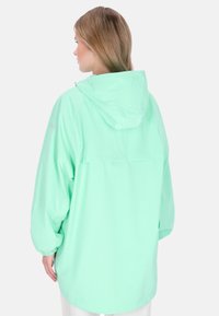 Mentaszínű vízálló kabát kapucnival és elasztikus mandzsettákkal, laza szabással és sima textúrával, kültéri használatra alkalmas.