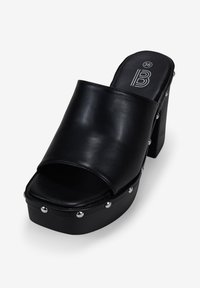 Sandalia plataforma negra con una parte superior de cuero ancho y tachuelas plateadas a lo largo del borde. Presenta un tacón bloque grueso y un diseño de punta abierta.