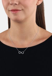 Collana d'infinito in argento su una catena sottile, con una finitura lucida e un sottile scintillio, indossata su una maglietta nera.