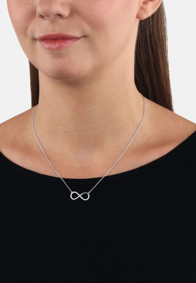 Collana d'infinito in argento su una catena sottile, con una finitura lucida e un sottile scintillio, indossata su una maglietta nera.