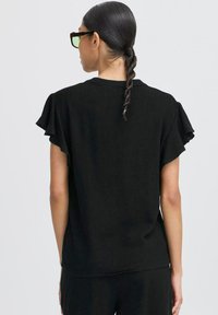 Top corto nero a maniche corte con una vestibilità rilassata. Presenta maniche arricciate e un collo pulito. Tessuto liscio con una leggera trama.