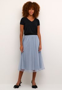 Fekete V nyakú póló, amelyet egy világoskék, könnyed, midi tüll szoknyával párosítottak. A szettet fekete, masnival díszített cipők egészítik ki.