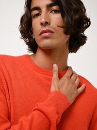 Oranje stickad tröja med rund hals; mjuk textur och långa ärmar. Hand placerad på axeln, med detaljer i ribbad mudd.