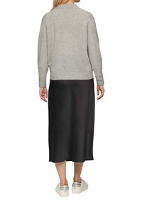 Hellgrauer Pullover mit geripptem Saum, kombiniert mit einem schwarzen Satin-Midirock. Weiße Sneakers mit silbernen Akzenten runden das Outfit ab.
