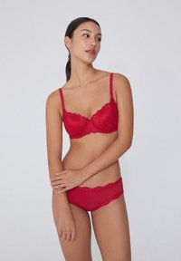 Červená krajková podprsenka a odpovídající kalhotky s vlnitými okraji. Měkká textura a nastavitelné ramínka, zdobené jemnými květinovými vzory.