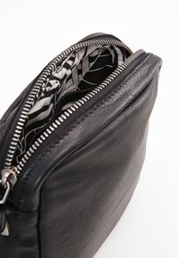 Svart läderpouch med texturerad yta, dragkedjestängning och ett mönstrat svart och vitt tyginrede.