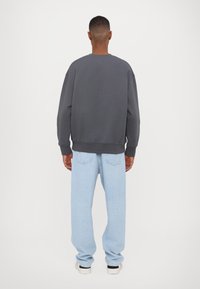 Donkergrijze sweatshirt met een relaxte pasvorm, ronde halslijn en geribde manchetten, gecombineerd met lichtblauwe jeans en witte sneakers.